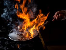 Side view mushroom frying with stove and fire and human hand in pan on black background