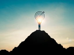 Silhouette of businessman holding target board on the top of mountain with over blue sky and sunlight. It is symbol of leadership successful achievement with goal and objective target.