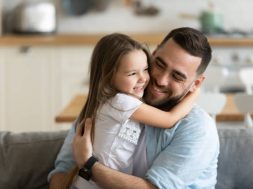 Close up smiling loving young father hugging adorable little daughter, enjoying tender moment, spending weekend together, sitting on cozy couch at home, good family relationship between dad and child