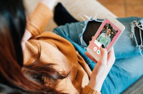 Young adult woman swiping on an online dating app. She's using her smart phone on the sofa at home.