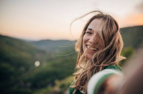 One woman, portrait of a young female hiker taking a selfie high on mountain in sunset.