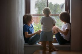 Happy siblings, boy brothers, sitting on a window shield on a rainy day, playing together, summertime