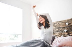 Cropped shot of a young woman stretching while sitting in her bed