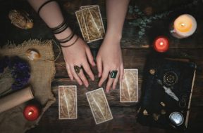 Tarot cards, magic book and fortune teller hands on a wooden table background. Future reading concept. Divination.