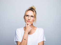 Thoughtful blond woman with hand on chin looking up against gray background